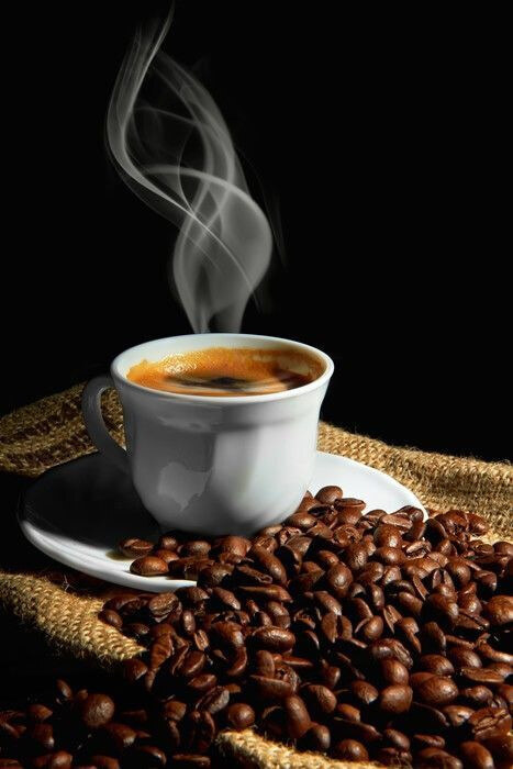 A cup of coffee with smoke on a saucer and beans A cup of coffee with smoke on a saucer and beans